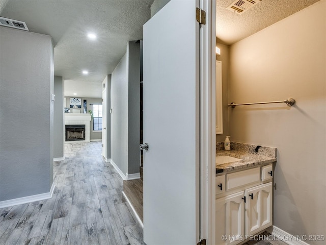 hallway featuring a textured ceiling, light wood-style flooring, visible vents, and baseboards