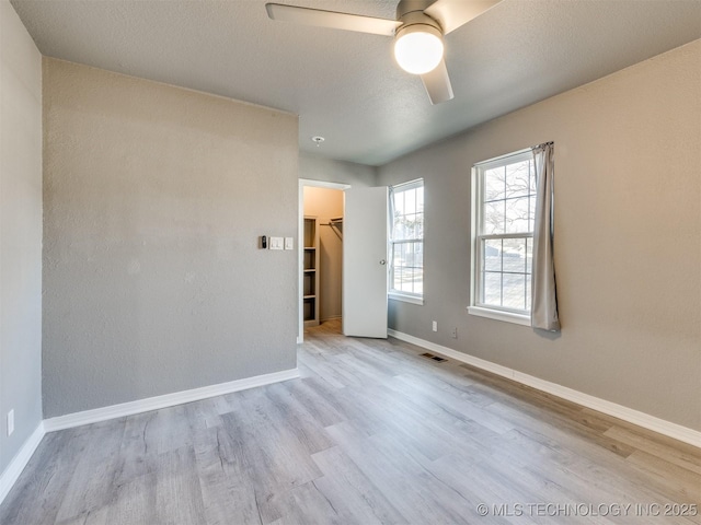 empty room with light wood finished floors, baseboards, visible vents, ceiling fan, and a textured ceiling