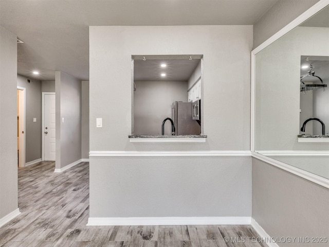 kitchen with stainless steel appliances, light wood-type flooring, a sink, and baseboards