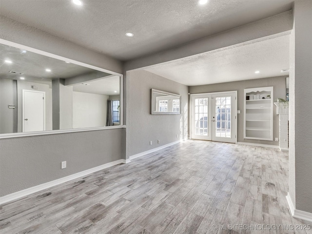 unfurnished room with french doors, a textured wall, light wood-style flooring, a textured ceiling, and baseboards