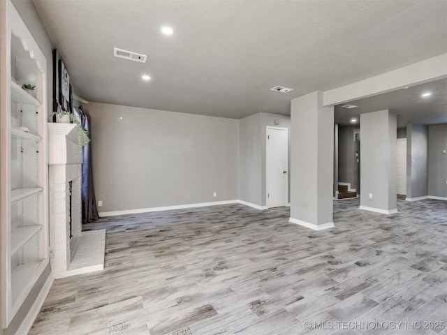 basement with a textured ceiling, a fireplace, visible vents, baseboards, and light wood-style floors