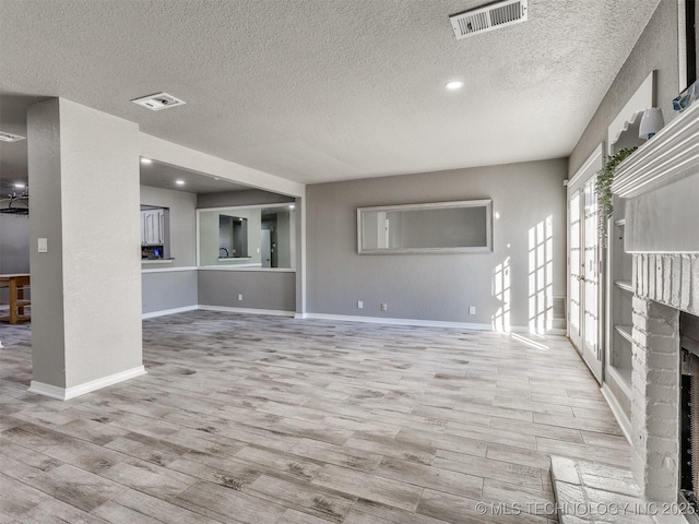 unfurnished living room featuring light wood-type flooring, a brick fireplace, and visible vents