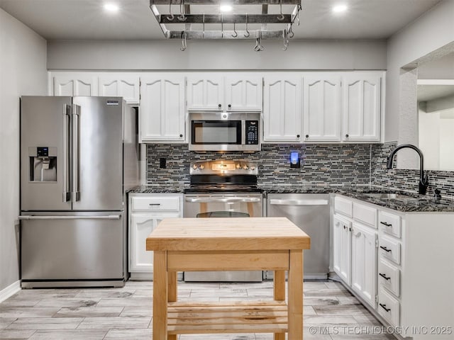 kitchen featuring stainless steel appliances, a sink, white cabinets, dark stone counters, and tasteful backsplash