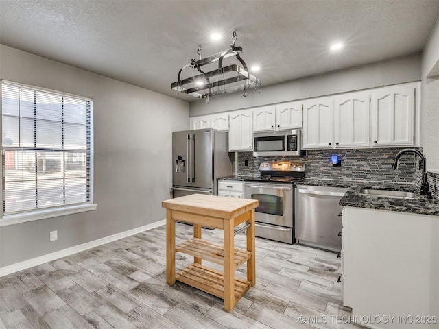 kitchen with light wood finished floors, stainless steel appliances, backsplash, white cabinetry, and a sink