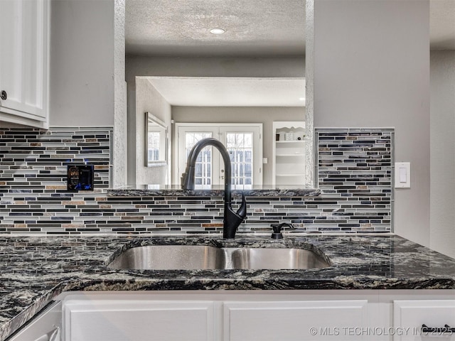 kitchen featuring tasteful backsplash, white cabinets, dark stone countertops, a textured ceiling, and a sink