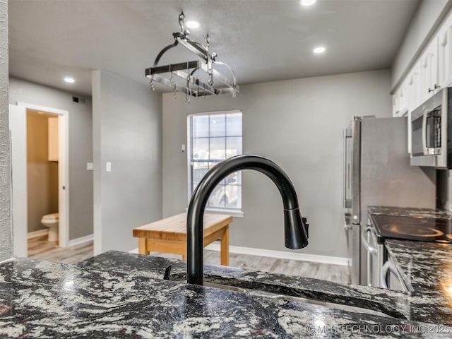 details with white cabinets, stainless steel microwave, light wood-style flooring, and dark stone countertops