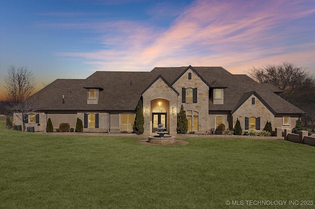 french provincial home featuring stone siding, a lawn, and roof with shingles