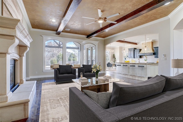 living room with arched walkways, ornamental molding, beam ceiling, and a high end fireplace