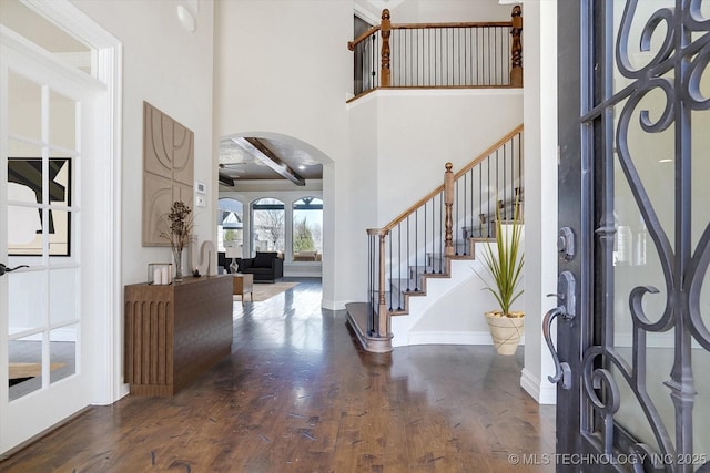 foyer entrance with arched walkways, baseboards, dark wood-style floors, stairs, and a high ceiling