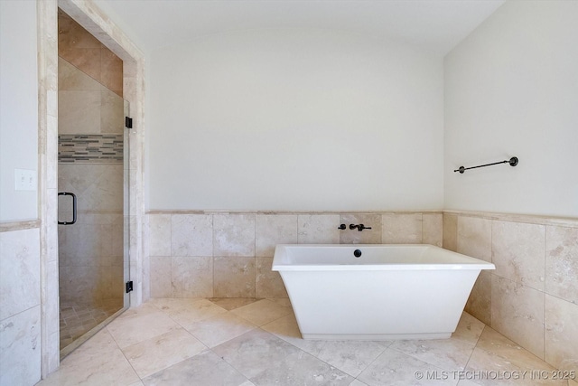 bathroom featuring a stall shower, a wainscoted wall, and tile walls