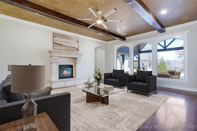 living room with baseboards, a glass covered fireplace, wood finished floors, crown molding, and beam ceiling