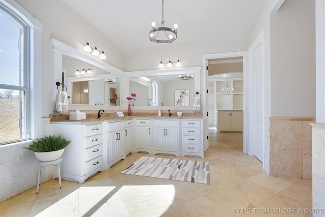 full bathroom with an inviting chandelier, tile patterned flooring, vaulted ceiling, vanity, and tile walls