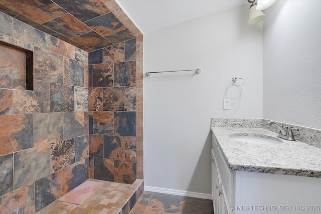 full bathroom with baseboards, tiled shower, and vanity