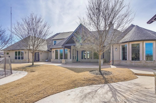 back of property featuring stone siding, a patio area, and a chimney