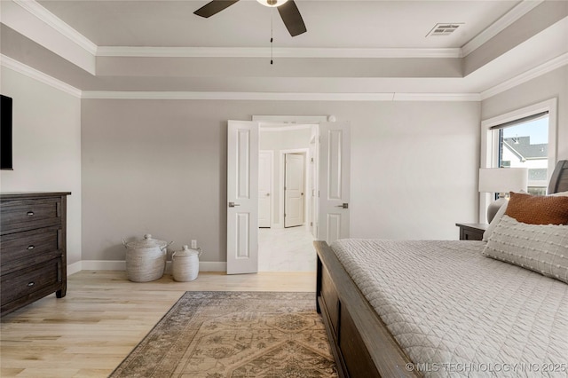 bedroom featuring light wood-style flooring, visible vents, baseboards, ornamental molding, and a raised ceiling