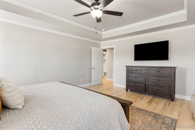 bedroom featuring a ceiling fan, baseboards, ornamental molding, light wood-type flooring, and a raised ceiling