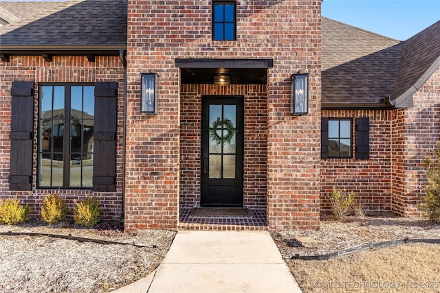 property entrance with a shingled roof and brick siding