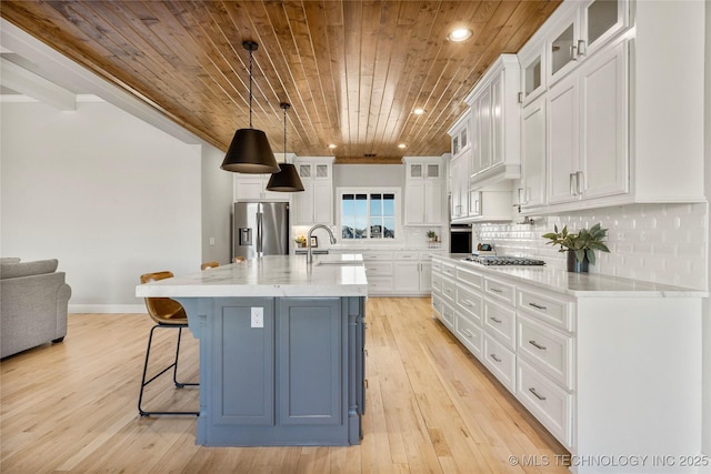 kitchen featuring a kitchen island with sink, appliances with stainless steel finishes, glass insert cabinets, and white cabinets