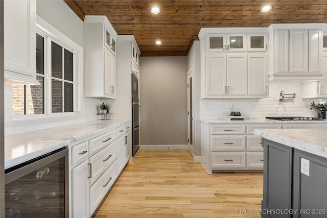 kitchen with wine cooler, glass insert cabinets, light wood-style floors, wood ceiling, and white cabinetry