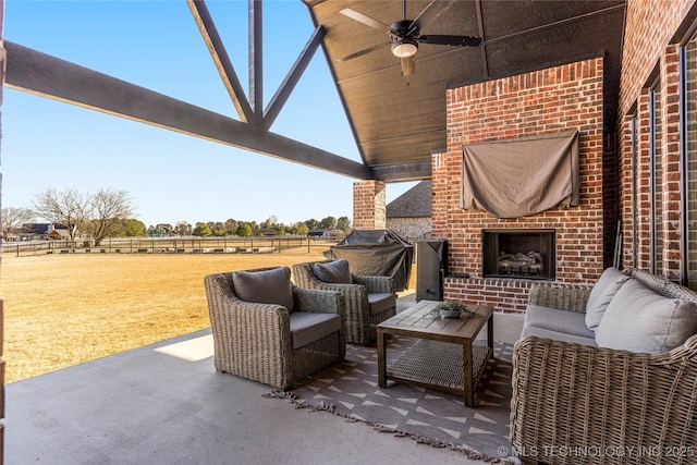 view of patio featuring an outdoor brick fireplace, fence, ceiling fan, and a rural view