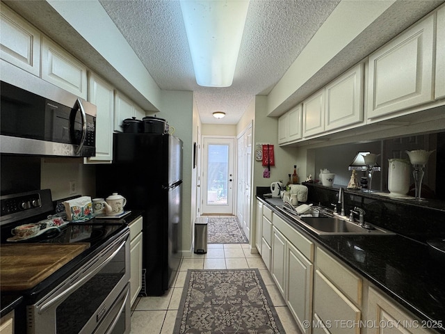 kitchen with a textured ceiling, stainless steel appliances, light tile patterned flooring, and a sink