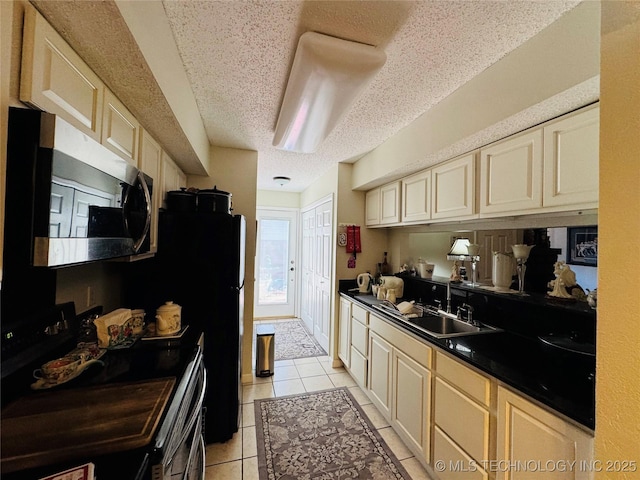 kitchen featuring a textured ceiling, black range with electric cooktop, light tile patterned flooring, a sink, and stainless steel microwave