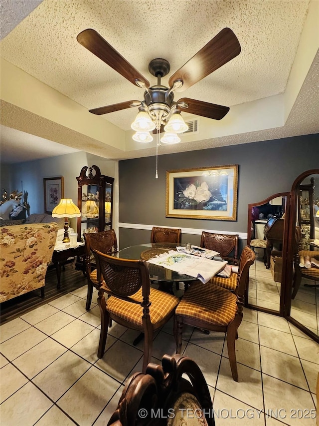 dining area with light tile patterned floors, a raised ceiling, and a textured ceiling