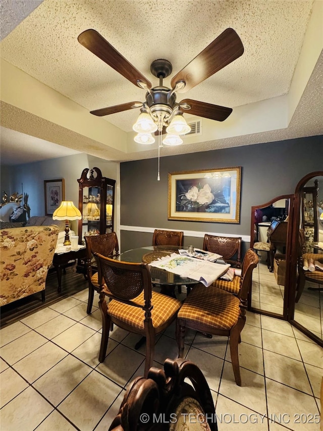 dining area featuring light tile patterned floors, a raised ceiling, and a textured ceiling