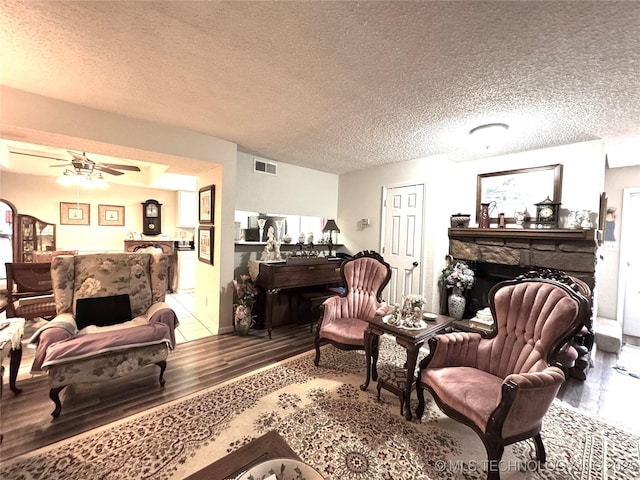 living area with a ceiling fan, a textured ceiling, wood finished floors, a fireplace, and visible vents