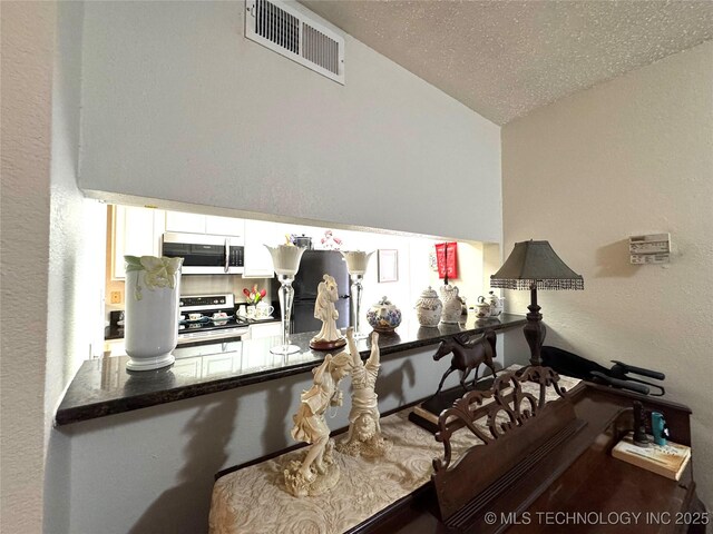 6371 S 80th E Ave Unit 6H, Tulsa, OK 74133 - kitchen featuring electric stove, white microwave, lofted ceiling, refrigerator, and a textured wall