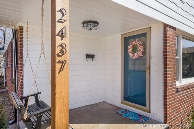 property entrance with a porch and brick siding