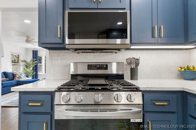 kitchen with appliances with stainless steel finishes, blue cabinets, ceiling fan, and tasteful backsplash