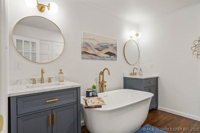 bathroom with wood finished floors, two vanities, a sink, a freestanding bath, and baseboards