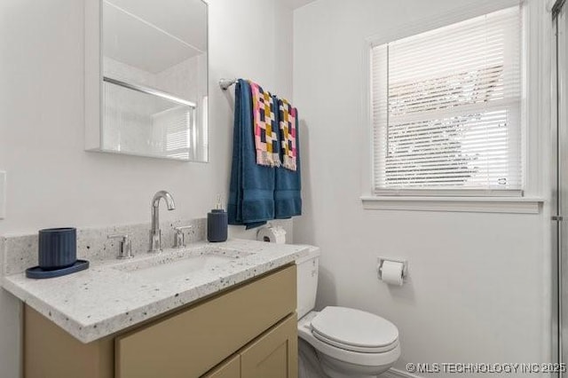 bathroom featuring toilet, vanity, and a shower with shower door