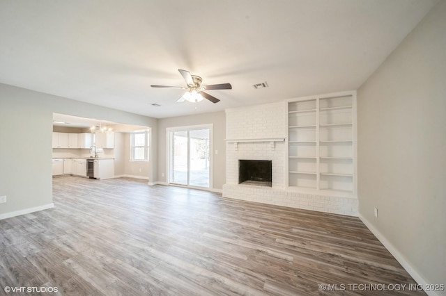 unfurnished living room with a brick fireplace, baseboards, and wood finished floors