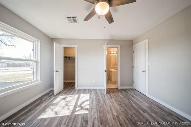 unfurnished bedroom featuring baseboards, visible vents, a walk in closet, and wood finished floors