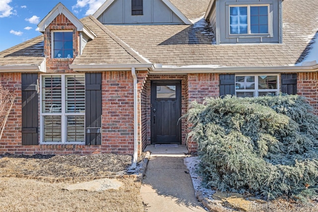 entrance to property featuring brick siding and roof with shingles