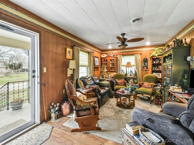 living room featuring a ceiling fan, visible vents, and wooden walls