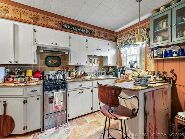 kitchen with light stone counters, white cabinetry, gas stove, glass insert cabinets, and pendant lighting