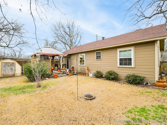 rear view of property with an outbuilding, a storage shed, a shingled roof, fence, and a gazebo