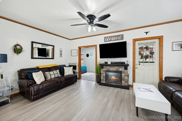 living area featuring light wood finished floors, baseboards, a ceiling fan, crown molding, and a stone fireplace