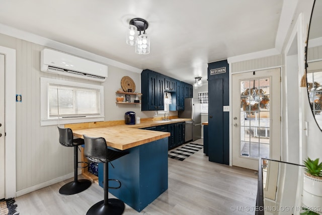 kitchen featuring a breakfast bar area, an AC wall unit, wood counters, blue cabinets, and a peninsula