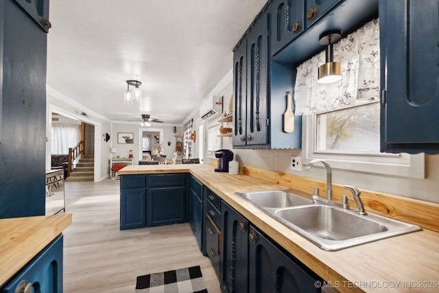 kitchen with a peninsula, an AC wall unit, blue cabinetry, pendant lighting, and a sink