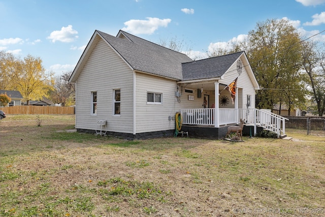 view of side of home featuring covered porch, a shingled roof, fence, and a lawn