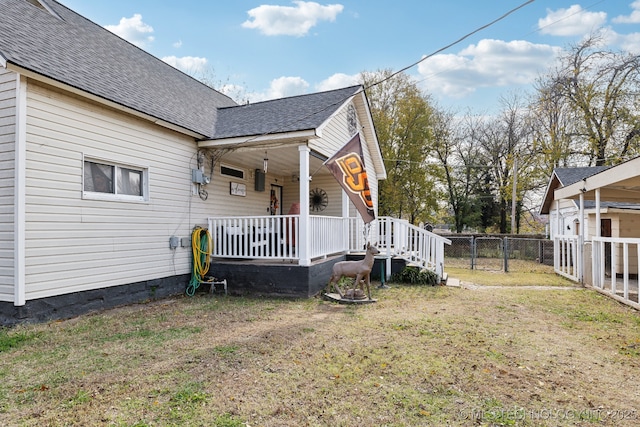 view of side of home with roof with shingles, a porch, a lawn, and fence