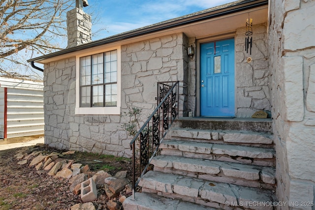 doorway to property featuring stone siding, a chimney, and fence