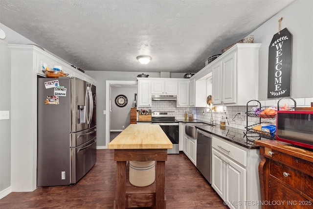 kitchen with under cabinet range hood, butcher block counters, white cabinetry, appliances with stainless steel finishes, and decorative backsplash