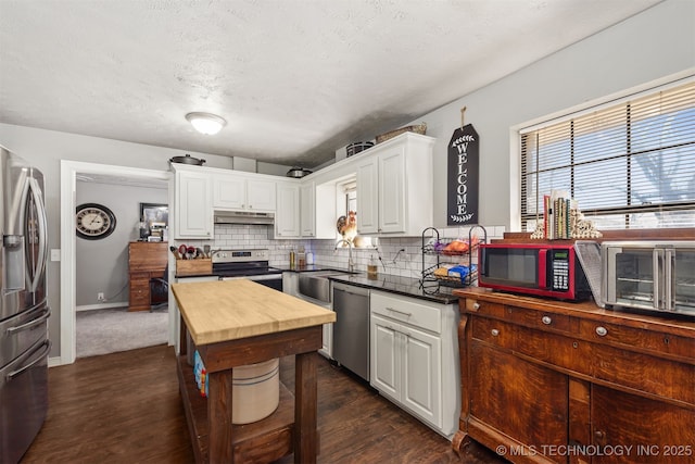 kitchen with stainless steel appliances, backsplash, white cabinetry, wood counters, and under cabinet range hood