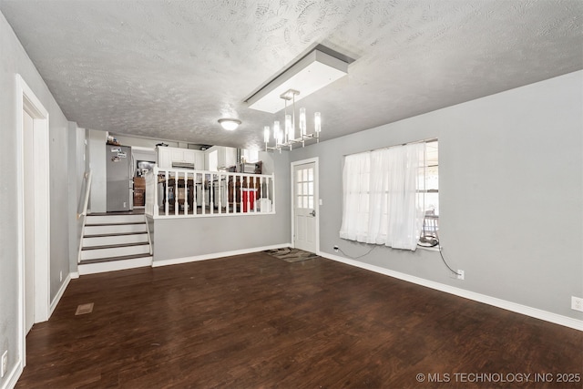 unfurnished room featuring baseboards, wood finished floors, stairs, a textured ceiling, and a chandelier