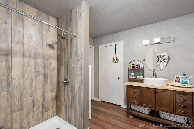 full bathroom with a textured ceiling, wood finished floors, a tile shower, and vanity